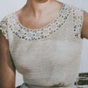 以下が含まれることがあります： クリーム色のクロシェ編みトップス。丸いネックラインとキャップスリーブが特徴。ネックラインと袖口には、詳細な花のレース模様があります。トップのボディは、きつく、質感のあるステッチです。