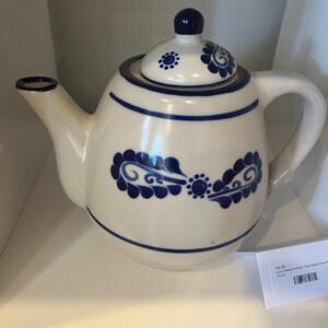 Könnte beinhalten: Eine weiße Teekanne aus Keramik mit einem blauen und weißen Blumenmuster. Die Teekanne hat einen runden Körper und einen Ausguss auf der linken Seite. Der Deckel ist ebenfalls mit einem blauen und weißen Blumenmuster verziert.