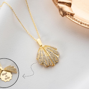 Puede incluir: Un collar de oro con un colgante de concha que se abre para revelar un espacio para grabar. El colgante está incrustado con pequeñas piedras transparentes. La grabación dice "Forever & Always".