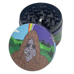 May include: A round metal herb grinder with a black interior featuring sharp teeth and a mesh screen. The lid displays a colorful illustration of a brown, furry creature smoking a cigarette against a landscape with a rainbow and a starry night sky.