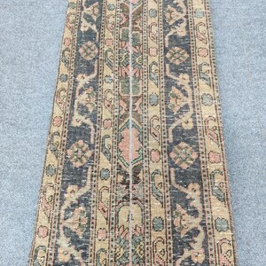 May include: A rectangular rug with a detailed, vintage design. The rug features a central stripe with floral and geometric patterns in shades of pink, green, and brown. The borders are dark blue with similar patterns.