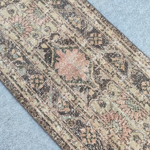 Könnte beinhalten: Ein Teppich im antiken Stil mit einem Used-Look. Der Teppich hat ein zentrales Blumenmedaillon in Pfirsich- und Brauntönen, umgeben von komplizierten Mustern in Beige, Braun und Türkis. Das Design des Teppichs ist symmetrisch und rechteckig.