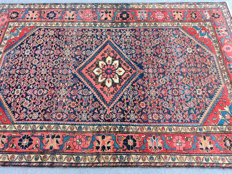 Peut inclure: Un tapis rectangulaire pr&eacute;sentant un champ central bleu fonc&eacute; avec un grand m&eacute;daillon en forme de losange contenant un motif floral en cr&egrave;me, rouge et bleu. Le tapis est encadr&eacute; par une large bordure rouge aux motifs floraux et g&eacute;om&eacute;triques.