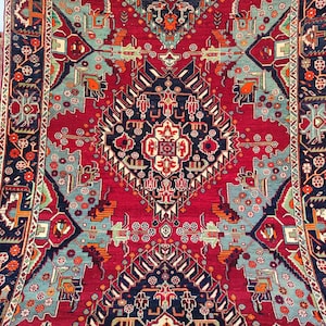 May include: A detailed rug with a central medallion design. The rug has a deep red background with geometric patterns in navy, teal, and orange. The border is dark navy with floral and geometric designs. The rug is likely made of wool.