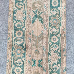 Könnte beinhalten: Ein rechteckiger Vintage-Teppich mit Used-Look. Er hat ein beiges Mittelfeld und türkisfarbene und beige Bordüren. Das Design umfasst florale und geometrische Muster in Türkis, Beige und Blautönen. Der Teppich ist wahrscheinlich aus Wolle oder einem ähnlichen Material.