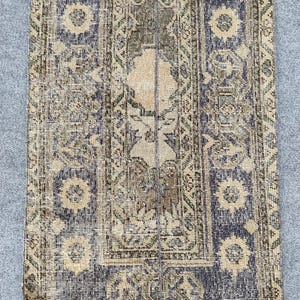 Könnte beinhalten: Ein rechteckiger Vintage-Teppich mit einem Used-Look. Der Teppich hat ein zentrales Design in Beige und Braun, das von dunkelblauen Bordüren mit floralen Mustern umrahmt wird. Die Farbpalette umfasst Beige-, Blau- und Grüntöne.