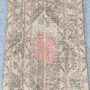 Könnte beinhalten: Ein rechteckiger, abgenutzter Teppich mit einem zentralen Medaillon-Design. Der Teppich weist eine Farbpalette aus gedämpften Grüntönen, Rosa- und Brauntönen mit komplizierten floralen und geometrischen Mustern auf. Die Kanten sind gefranst, was zur Vintage-Ästhetik beiträgt.