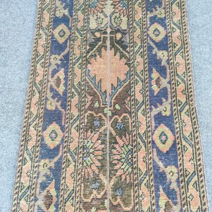 May include: A rectangular rug with a central design of peach and brown floral patterns, flanked by navy blue borders with geometric shapes. The rug has a vintage, distressed look.