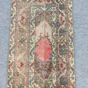 Könnte beinhalten: Rechteckiger Vintage-Teppich mit abgenutztem Aussehen. Der Teppich hat ein zentrales Rautenmuster in Rot und Beige, umgeben von komplizierten Mustern in Blau, Grün und Braun. Der Rand ist hellbeige mit sich wiederholenden geometrischen Formen.