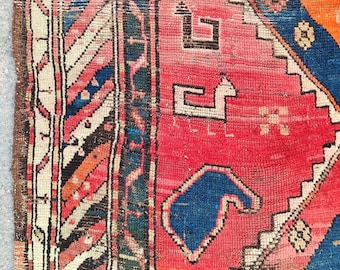 May include: Close-up of a section of a vintage rug with a complex geometric design. The rug features a vibrant color palette including red, blue, orange, and white. The pattern includes stylized shapes and borders.