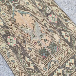 Könnte beinhalten: Ein antiker Teppich mit abgenutztem, verblasstem Aussehen. Der Teppich hat ein zentrales Design in Beige und Hellblau, umgeben von einem dunkelbraunen Rand mit floralen und geometrischen Mustern. Die Farbpalette umfasst Grün-, Braun- und Rosatöne.