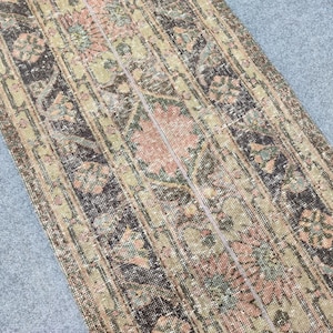 Peut inclure: Un tapis ancien d'aspect vieilli. Le tapis présente un motif répétitif de motifs floraux et géométriques dans des tons de marron, de vert et de rose. Le design du tapis est symétrique et a un aspect usé.