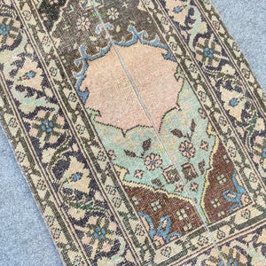 Può includere: Un tappeto antico con un motivo a medaglione centrale nei toni del marrone, pesca e verde acqua. Il tappeto presenta intricati motivi floreali e geometrici all'interno di un bordo dettagliato. L'aspetto usurato del tappeto suggerisce che sia vintage.