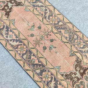 May include: A vintage runner rug with a central peach field and detailed floral patterns. The rug has a border with dark blue and beige accents, suitable for hallways or entryways. The rug's design is reminiscent of traditional styles.