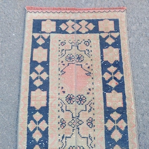 Könnte beinhalten: Ein rechteckiger Teppich im Vintage-Stil mit einem zentralen Design in Pfirsich und Beige, umrahmt von marineblauen Bordüren. Der Teppich weist geometrische und florale Muster mit einem Fransenrand auf. Der Teppich ist wahrscheinlich aus gewebtem Material.