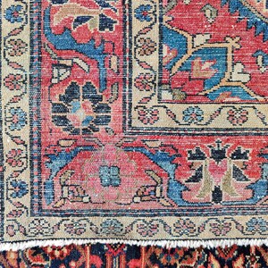 Peut inclure: Un tapis tiss&eacute; pr&eacute;sentant un motif g&eacute;om&eacute;trique et floral complexe dans des tons de rouge, bleu, beige et noir. Le design comprend un champ central avec des motifs complexes, entour&eacute; d'une large bordure avec des &eacute;l&eacute;ments floraux et des franges.