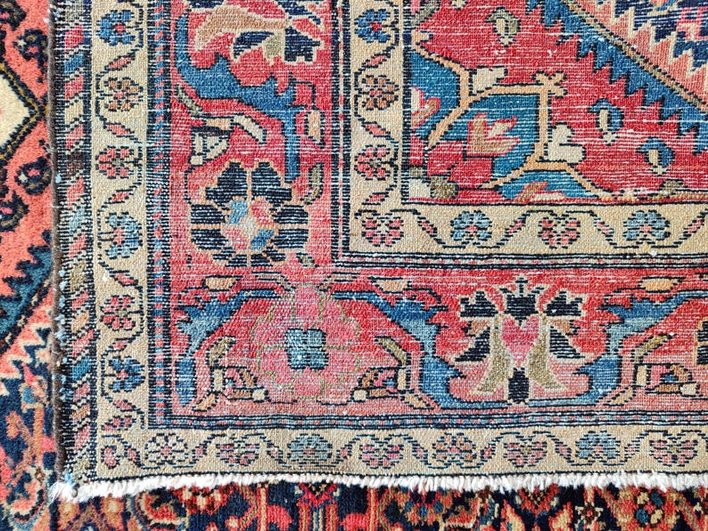 Peut inclure: Un tapis tiss&eacute; pr&eacute;sentant un motif g&eacute;om&eacute;trique et floral complexe dans des tons de rouge, bleu, beige et noir. Le design comprend un champ central avec des motifs complexes, entour&eacute; d'une large bordure avec des &eacute;l&eacute;ments floraux et des franges.