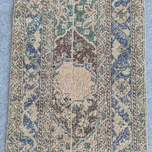 Könnte beinhalten: Ein rechteckiger Vintage-Teppich mit einem Used-Look. Er hat ein beiges Mittelfeld mit detaillierten geometrischen Mustern in Braun, Blau und Grün. Die Ränder sind gemustert und bilden ein zusammenhängendes Design. Der Stil deutet auf ein antikes Objekt hin.