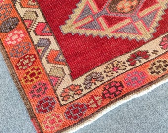 May include: Close-up of a section of a red, orange, and beige patterned rug. The rug features a central geometric design in red and beige, surrounded by a border with floral and geometric patterns in orange, pink, and brown.