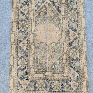 Könnte beinhalten: Ein rechteckiger Teppich im Vintage-Stil mit einem zentralen Medaillon-Design. Der Teppich hat einen beigen Hintergrund mit komplizierten Mustern in Marineblau, Olivgrün und Hauch von Rosa. Der Rand hat ein sich wiederholendes geometrisches Motiv.