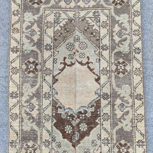 May include: Rectangular rug with a central medallion design. The rug features a beige background with a brown and grey border. Floral and geometric patterns are woven throughout, with accents of blue and green.
