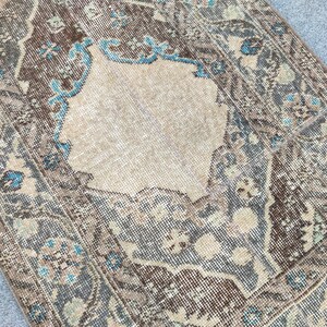 May include: A distressed, vintage-style rug with a central beige medallion and a border featuring floral patterns in shades of brown, blue, and grey. The rug has a worn appearance, adding to its character.