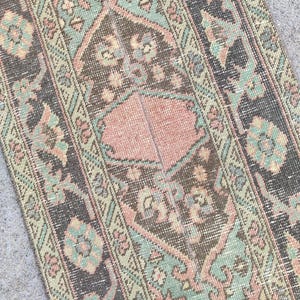 May include: A vintage rug with a worn, faded look. The rug has a central design in pink and brown, framed by borders in teal, green, and black. The pattern includes floral and geometric motifs.