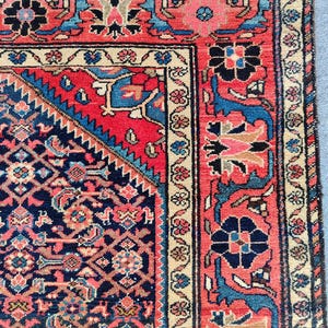 Peut inclure: Un tapis rectangulaire pr&eacute;sentant un champ central bleu marine fonc&eacute; avec un motif floral g&eacute;om&eacute;trique dense en rouge, bleu clair et cr&egrave;me. Le tapis poss&egrave;de une large bordure rouge &agrave; motifs floraux et un bord ext&eacute;rieur cr&egrave;me avec des fleurs.
