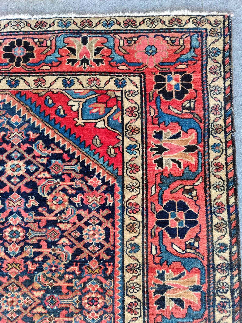 Peut inclure: Un tapis rectangulaire pr&eacute;sentant un champ central bleu marine fonc&eacute; avec un motif floral g&eacute;om&eacute;trique dense en rouge, bleu clair et cr&egrave;me. Le tapis poss&egrave;de une large bordure rouge &agrave; motifs floraux et un bord ext&eacute;rieur cr&egrave;me avec des fleurs.
