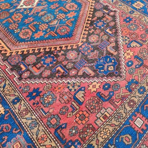 May include: Close-up of a traditional rug with a detailed geometric pattern. The rug features a central design in shades of blue, red, and brown, with intricate borders and a textured appearance. The rug's design includes floral and geometric motifs.