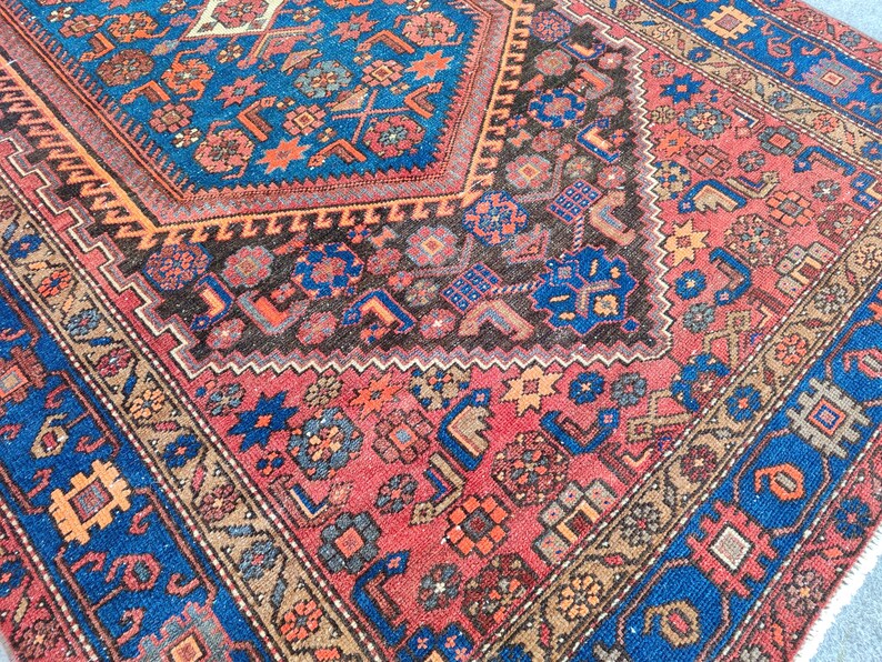May include: Close-up of a traditional rug with a detailed geometric pattern. The rug features a central design in shades of blue, red, and brown, with intricate borders and a textured appearance. The rug's design includes floral and geometric motifs.