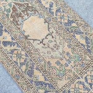 May include: An antique-style rug with a central beige medallion and intricate borders. The rug features a palette of blue, green, brown, and peach tones. The design includes floral and geometric patterns, creating a vintage aesthetic.