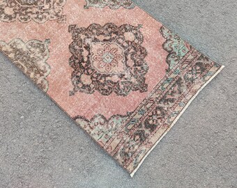 May include: A rectangular, distressed rug with a faded pink central field and ornate, dark brown and teal border and central medallion. The rug has a vintage, antique aesthetic.