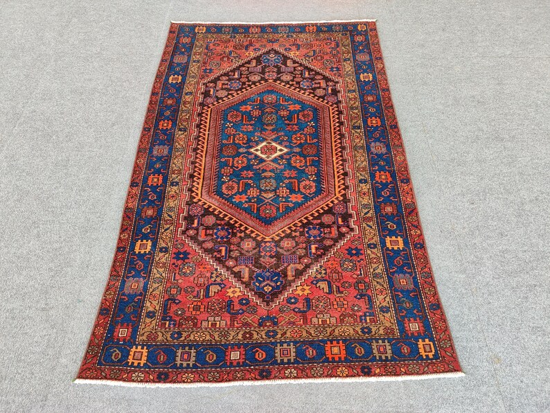May include: A rectangular, hand-knotted rug with an intricate geometric design. The rug features a central medallion in shades of blue, brown, and red, surrounded by a border of blue and orange. The rug's dimensions are not visible in the image.