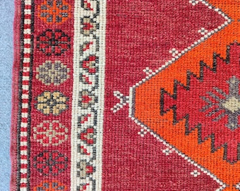 May include: Close-up of a section of a red, orange, and beige patterned rug. The rug features geometric designs and floral motifs. The border has a repeating pattern of small flowers and shapes.