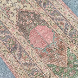 May include: An antique rug with a distressed, faded appearance. The rug features a central medallion in shades of pink and brown, surrounded by a border with floral and geometric patterns in muted tones of green, beige, and pink. The rug has a vintage, worn look.