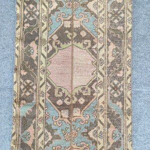 May include: A rectangular, vintage-style rug with a central pink panel and intricate geometric patterns in shades of brown, teal, and beige. The rug features a distressed look, suggesting it is an antique or a reproduction.
