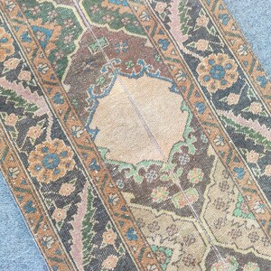 May include: An antique rug featuring a central beige medallion and detailed floral designs in brown, blue, orange, and green. The rug has a distressed, vintage look, with a faded colour palette and signs of wear.
