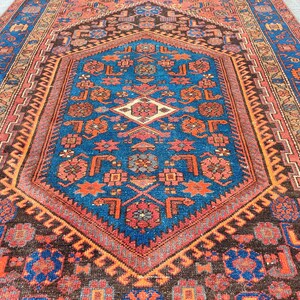May include: An intricately patterned rug with a central blue medallion, surrounded by a border of red, orange, and brown. The rug features geometric designs and floral motifs, creating a rich and detailed visual texture.