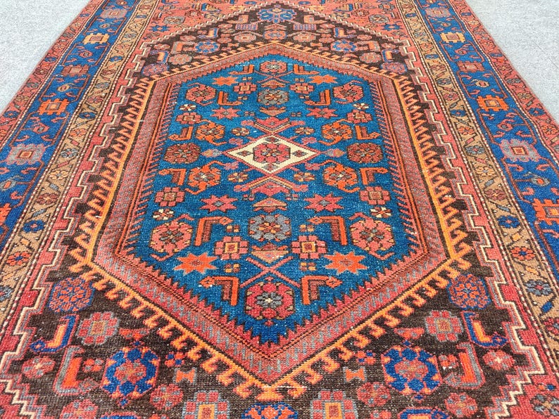 May include: An intricately patterned rug with a central blue medallion, surrounded by a border of red, orange, and brown. The rug features geometric designs and floral motifs, creating a rich and detailed visual texture.