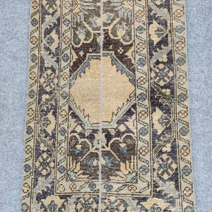 May include: A rectangular vintage rug featuring a central beige diamond design and detailed floral and geometric patterns in navy, brown, and sage green. The rug has a distressed, antique appearance.