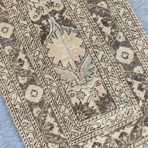 Könnte beinhalten: Ein rechteckiger Teppich im Used-Look mit einem zentralen Blumendesign und sich wiederholenden geometrischen Mustern. Der Teppich weist eine Farbpalette aus Braun-, Beige- und gedeckten Grüntönen auf, die eine Vintage-Ästhetik erzeugt. Das Design umfasst florale und geometrische Motive.