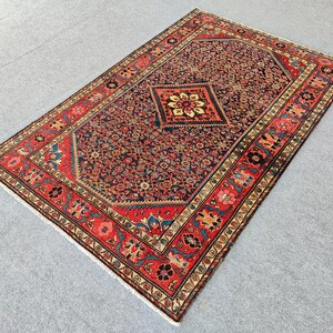 Peut inclure: Un tapis rectangulaire pr&eacute;sentant un champ central bleu fonc&eacute; orn&eacute; de motifs floraux complexes et d'un m&eacute;daillon central en forme de losange. Le tapis est encadr&eacute; par une large bordure rouge d&eacute;cor&eacute;e de motifs floraux et g&eacute;om&eacute;triques r&eacute;p&eacute;t&eacute;s.