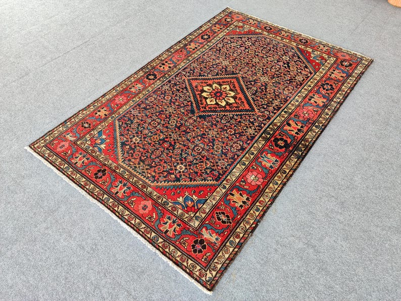 Peut inclure: Un tapis rectangulaire pr&eacute;sentant un champ central bleu fonc&eacute; orn&eacute; de motifs floraux complexes et d'un m&eacute;daillon central en forme de losange. Le tapis est encadr&eacute; par une large bordure rouge d&eacute;cor&eacute;e de motifs floraux et g&eacute;om&eacute;triques r&eacute;p&eacute;t&eacute;s.