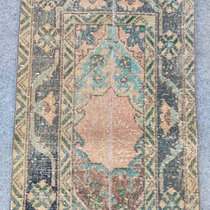 Op de afbeelding: Een rechthoekig vintage vloerkleed met een centraal medaillonontwerp. Het vloerkleed heeft een kleurenpalet van gedempte blauw-, groen-, perzik- en bruintinten. De rand heeft geometrische patronen en het vloerkleed heeft een antieke uitstraling.