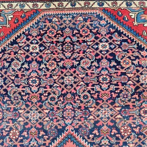Peut inclure: Un tapis rectangulaire pr&eacute;sentant un champ central bleu fonc&eacute; avec un motif g&eacute;om&eacute;trique dense et r&eacute;p&eacute;titif dans des tons de rose, bleu clair et cr&egrave;me. Le tapis est encadr&eacute; par une large bordure rouge avec des accents bleus et un bord ext&eacute;rieur cr&egrave;me.