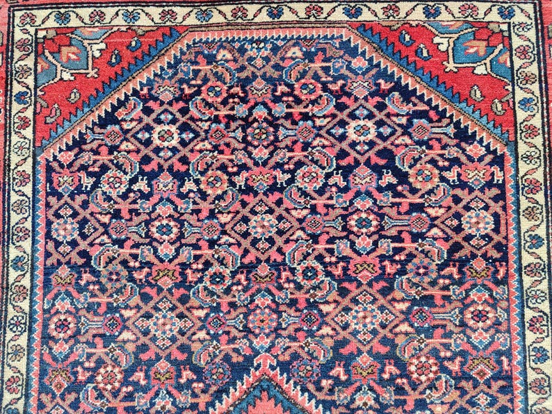 Peut inclure: Un tapis rectangulaire pr&eacute;sentant un champ central bleu fonc&eacute; avec un motif g&eacute;om&eacute;trique dense et r&eacute;p&eacute;titif dans des tons de rose, bleu clair et cr&egrave;me. Le tapis est encadr&eacute; par une large bordure rouge avec des accents bleus et un bord ext&eacute;rieur cr&egrave;me.