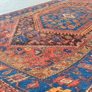 May include: An intricately patterned rug with a central medallion design. The rug features a rich color palette of red, blue, brown, and gold. The detailed patterns include geometric shapes and floral motifs, creating a traditional aesthetic.