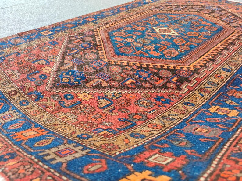 May include: An intricately patterned rug with a central medallion design. The rug features a rich color palette of red, blue, brown, and gold. The detailed patterns include geometric shapes and floral motifs, creating a traditional aesthetic.