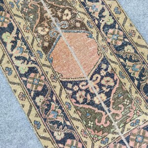 May include: A section of a vintage rug with a central peach-coloured medallion and floral patterns. The rug features a beige border with navy blue and olive green accents. The design includes pink, blue, and brown floral motifs.